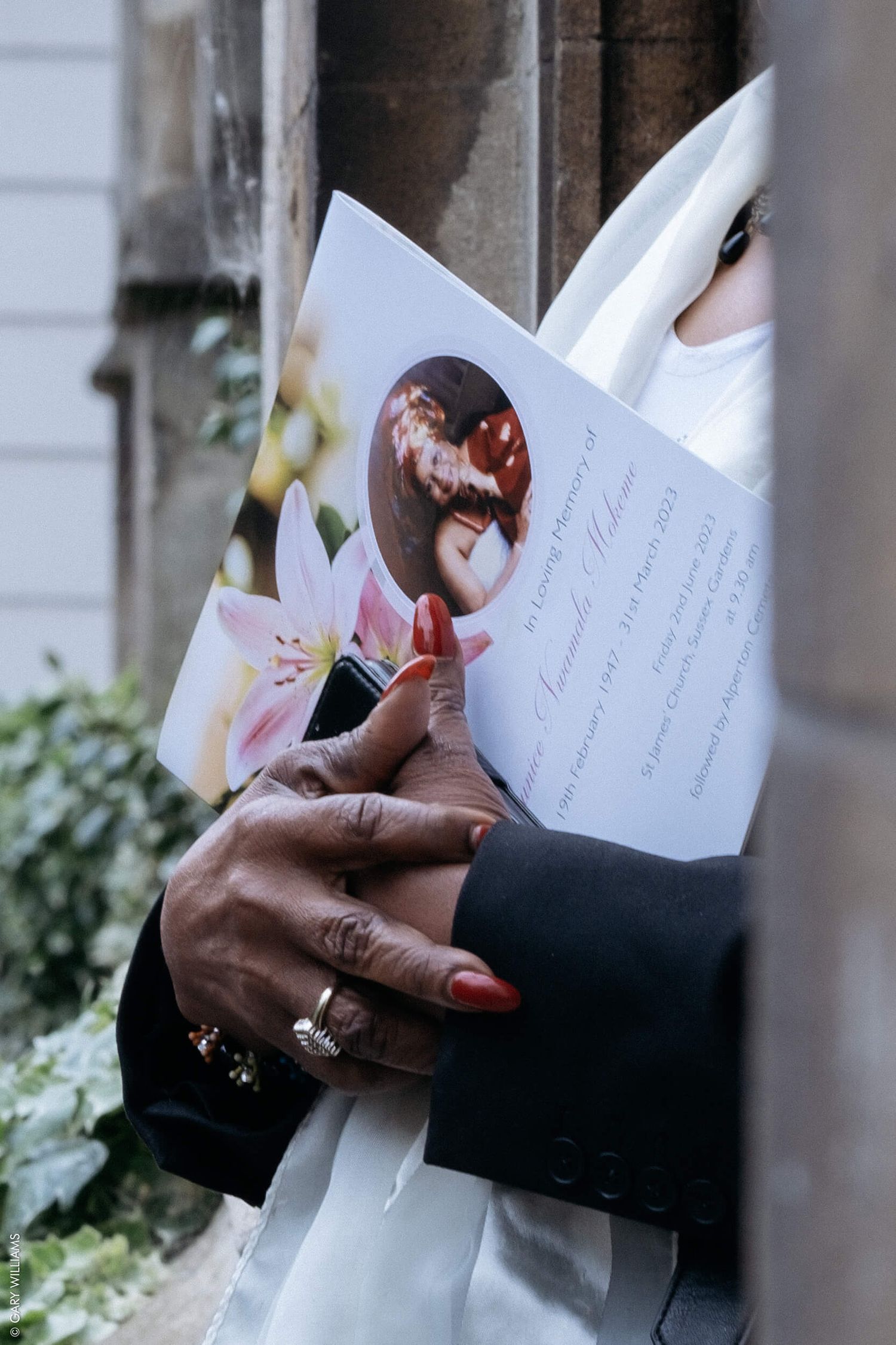 Hands holding a funeral program with floral decorations in the background.