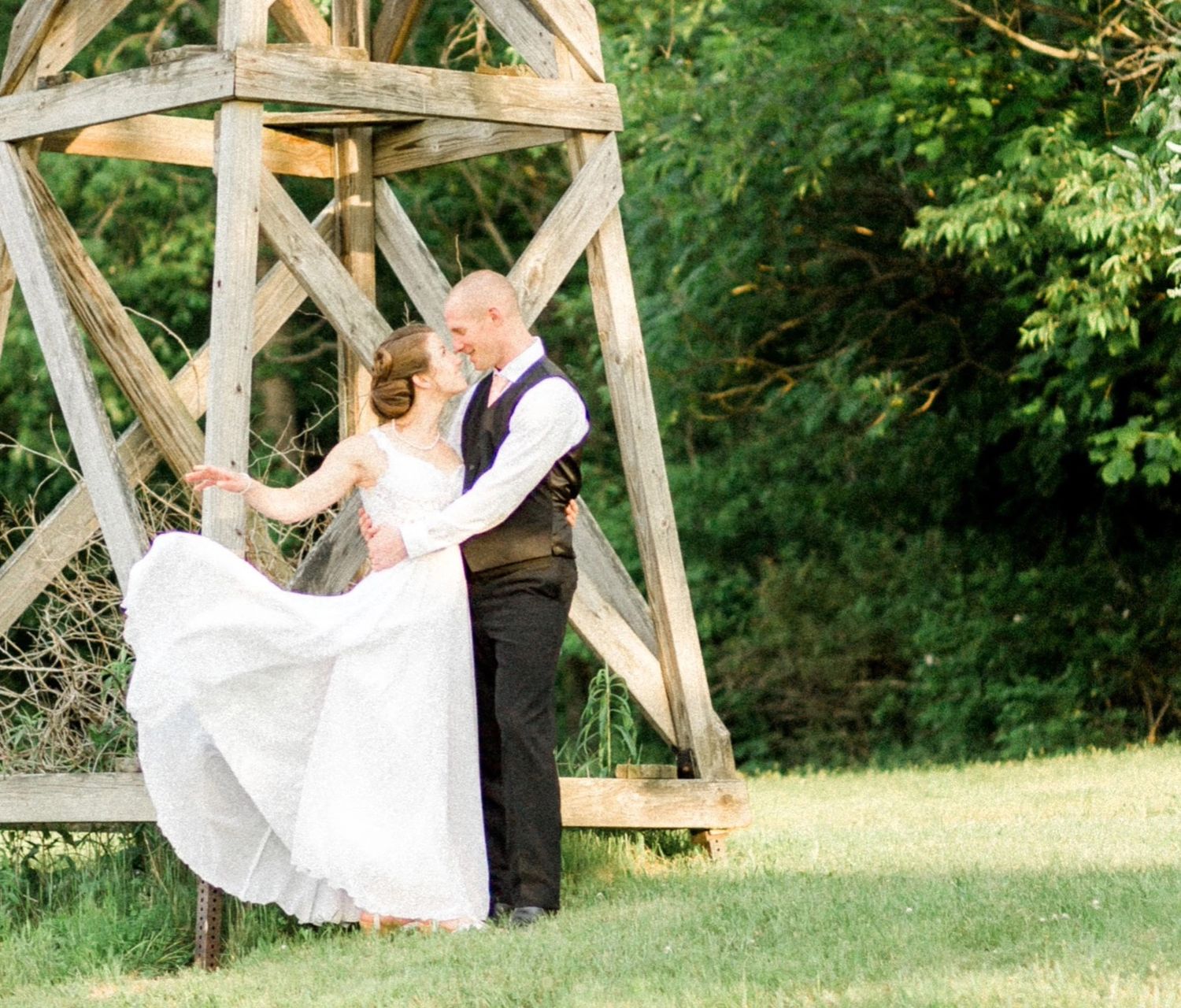 A couple dances together near a rustic wooden structure in a garden setting.