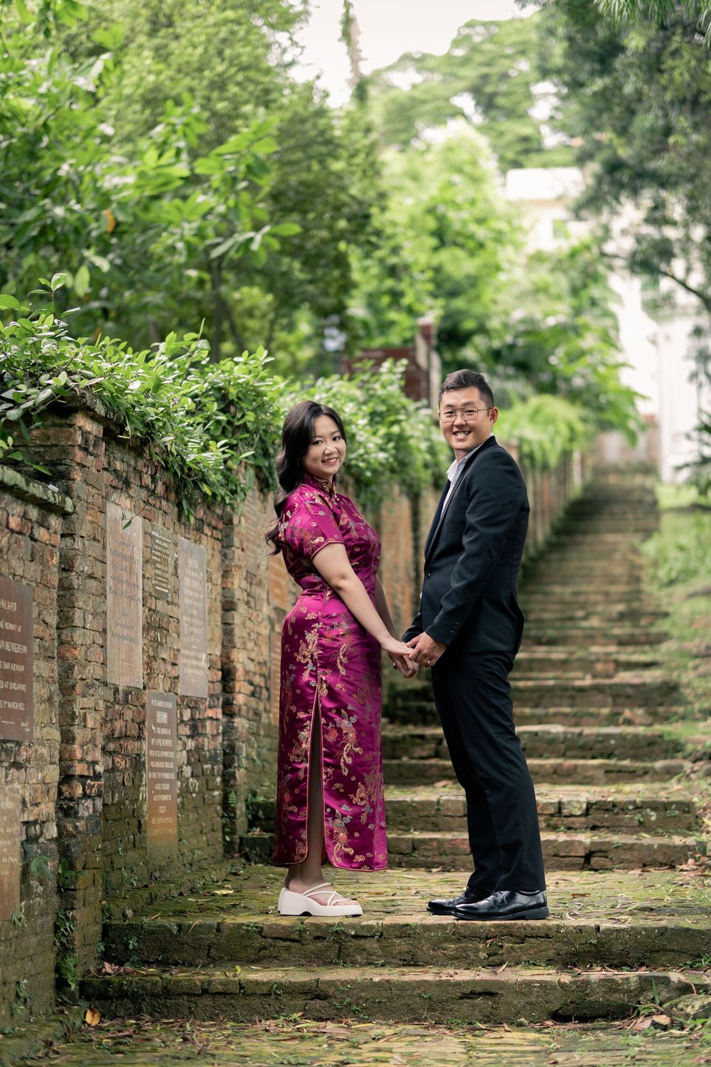 Couple posing on stone steps surrounded by lush greenery and brick walls.