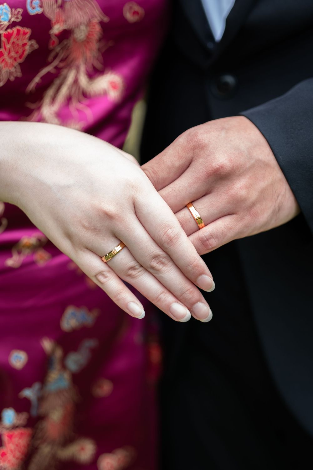 Close-up of matching gold wedding rings on couple's hands against pink traditional dress.