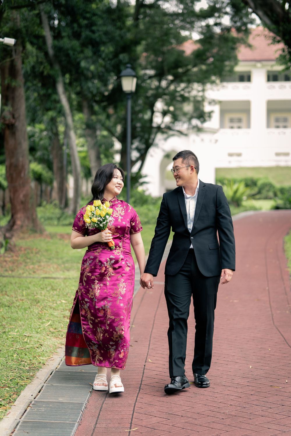 Couple walking together on a garden path, with bride wearing traditional pink cheongsam dress.