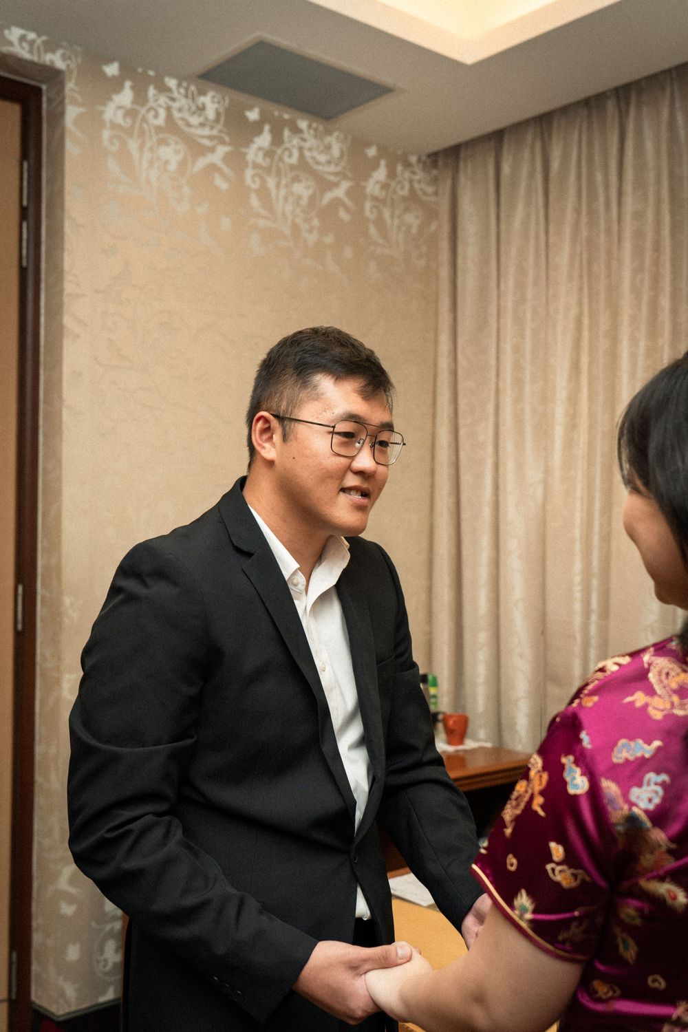 A couple having a conversation in a room with ornate wallpaper and curtains.