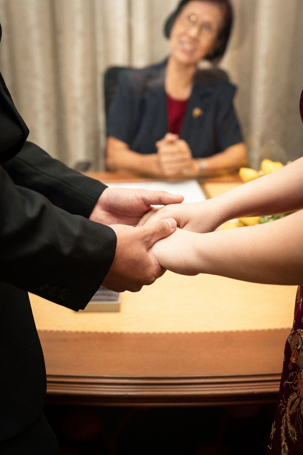 Close-up of hands clasped together during a ceremony with witness in background.