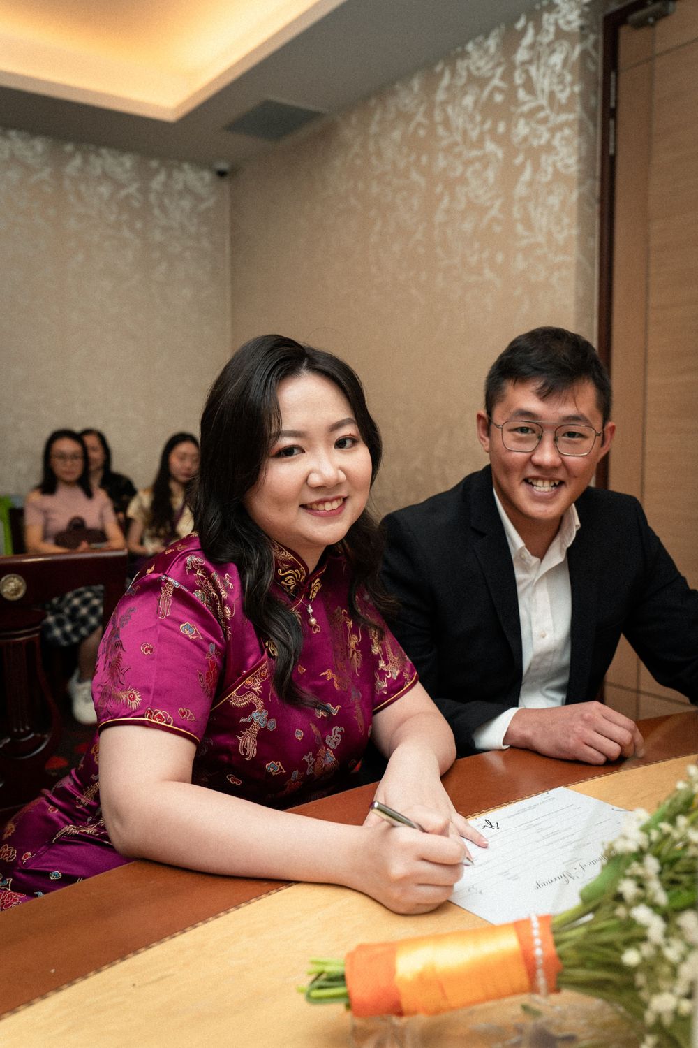 Two people signing documents at a wooden table during a ceremony.