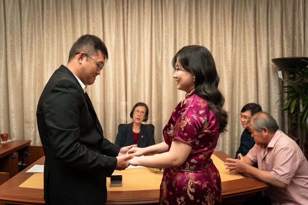 A traditional Chinese tea ceremony exchange between wedding guests in formal attire.