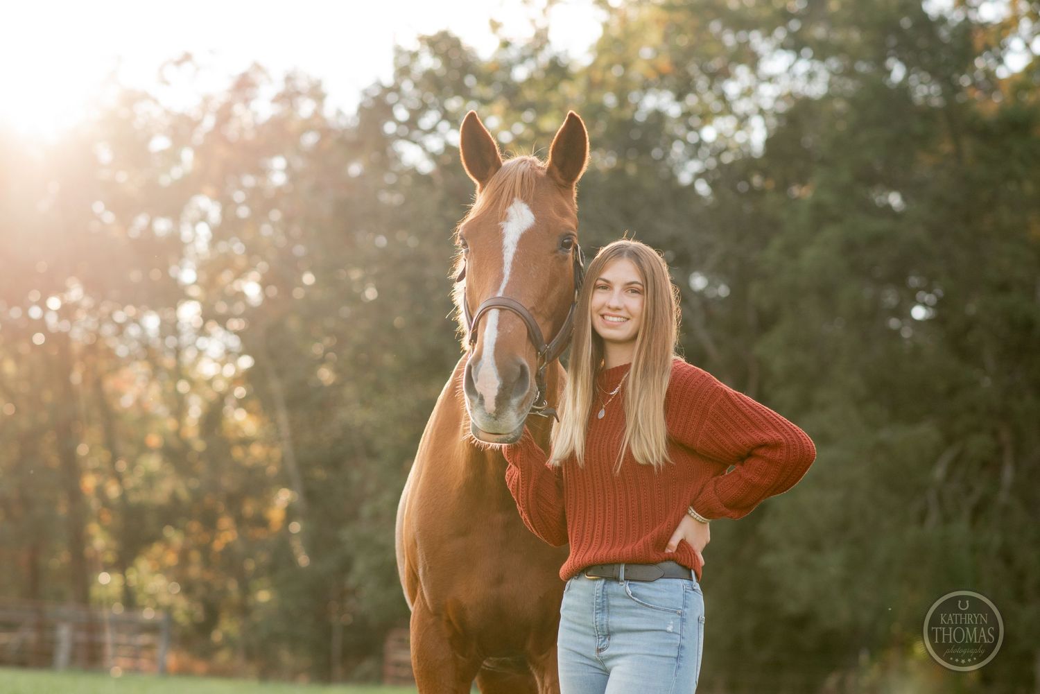 Golden sunlight illuminates a horse and companion in a red sweater against a wooded background.