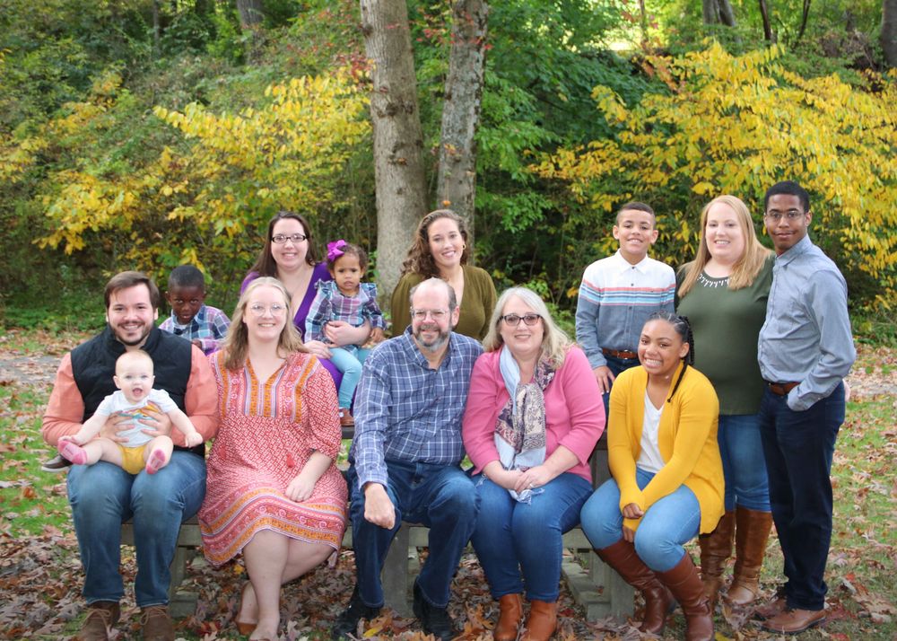 Large extended family group sits together on fallen log with autumn trees in background.