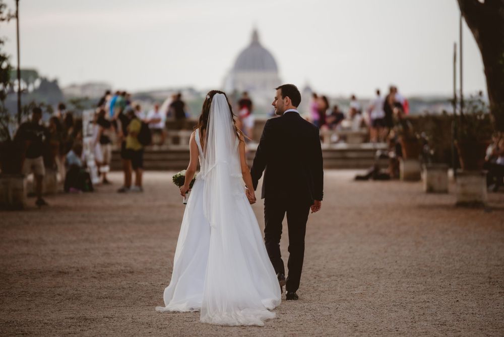 A wedding couple strolls along a scenic promenade with city views in the background.