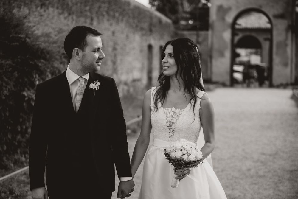 A wedding couple walks together on the grounds of a historic stone building.