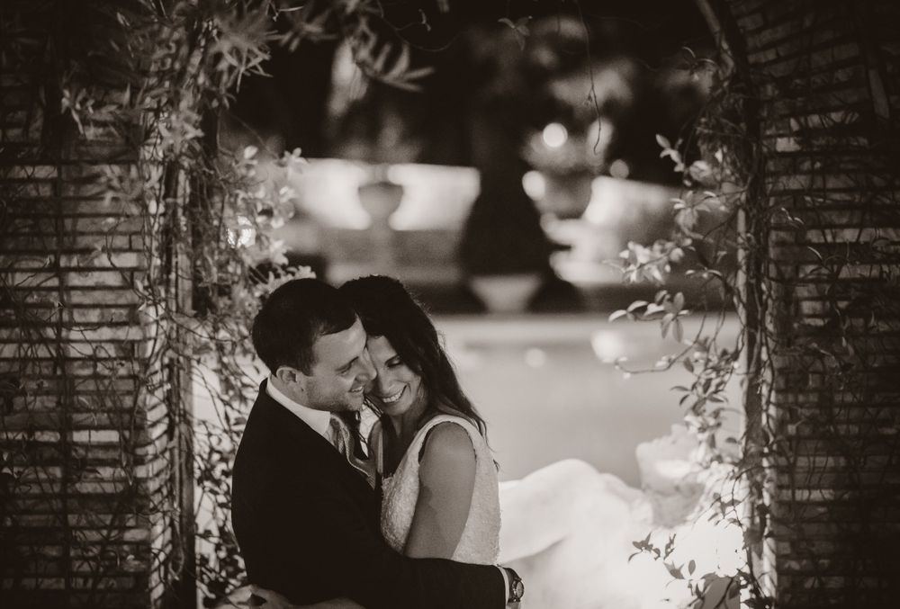 An intimate black and white wedding portrait framed by hanging vines and architectural elements.