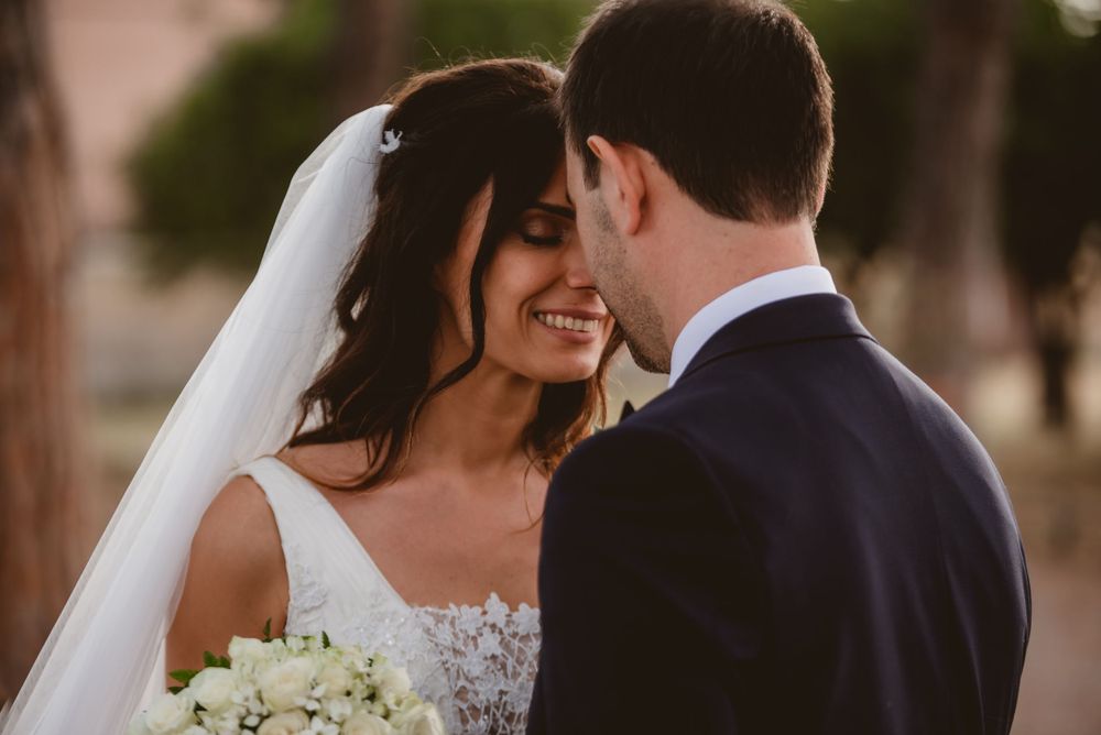 A romantic moment between newlyweds with white floral bouquet against natural scenery.