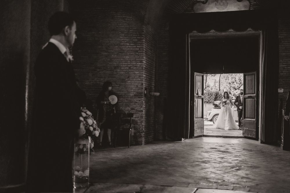 A dramatic black and white wedding photo captured in a dark brick corridor with natural lighting.