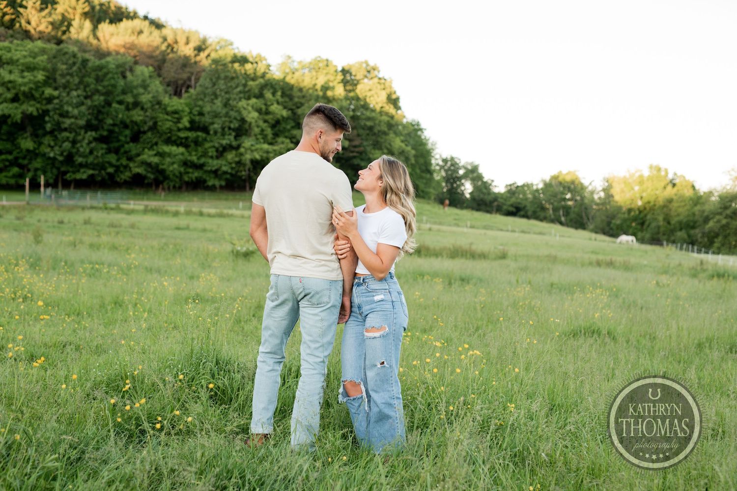 Couple in casual wear standing together on a green hillside during golden hour.