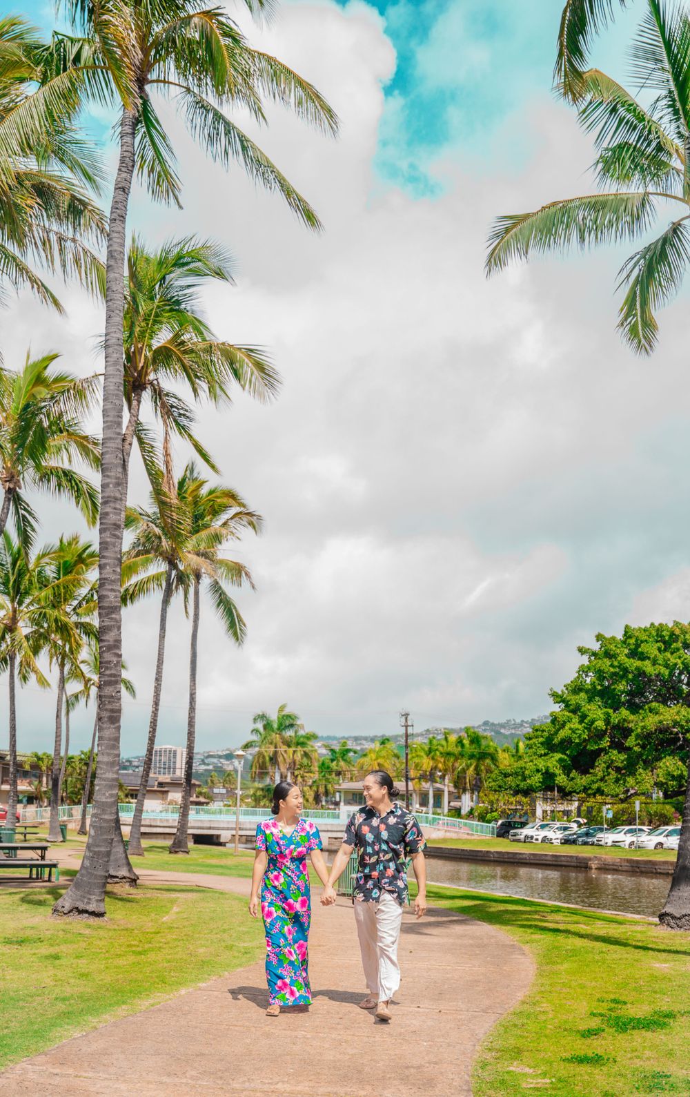 A couple takes a romantic walk along a palm-lined pathway under bright blue tropical skies.