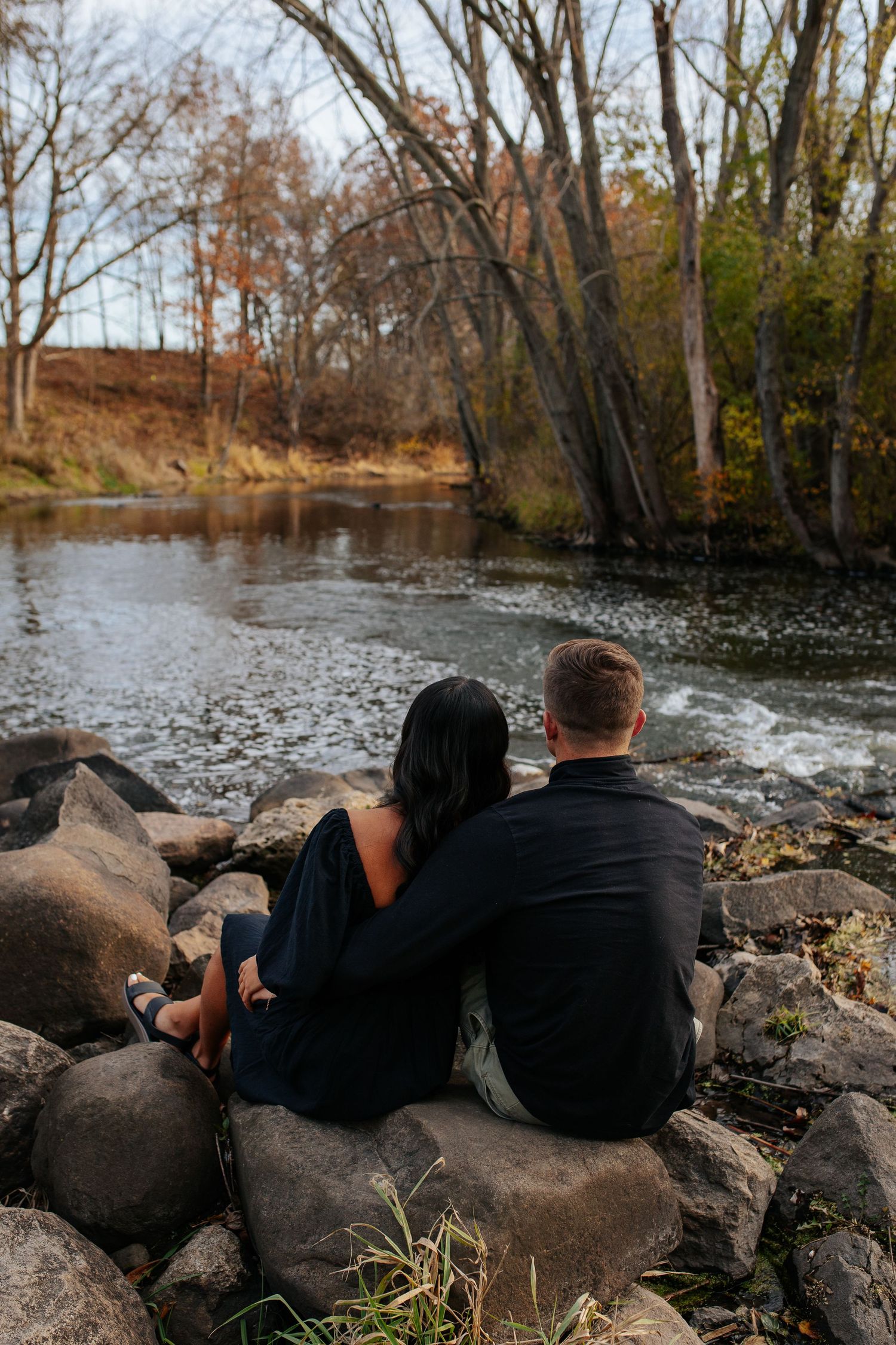 Two people relaxing on rocky riverbank while enjoying scenic autumn views.