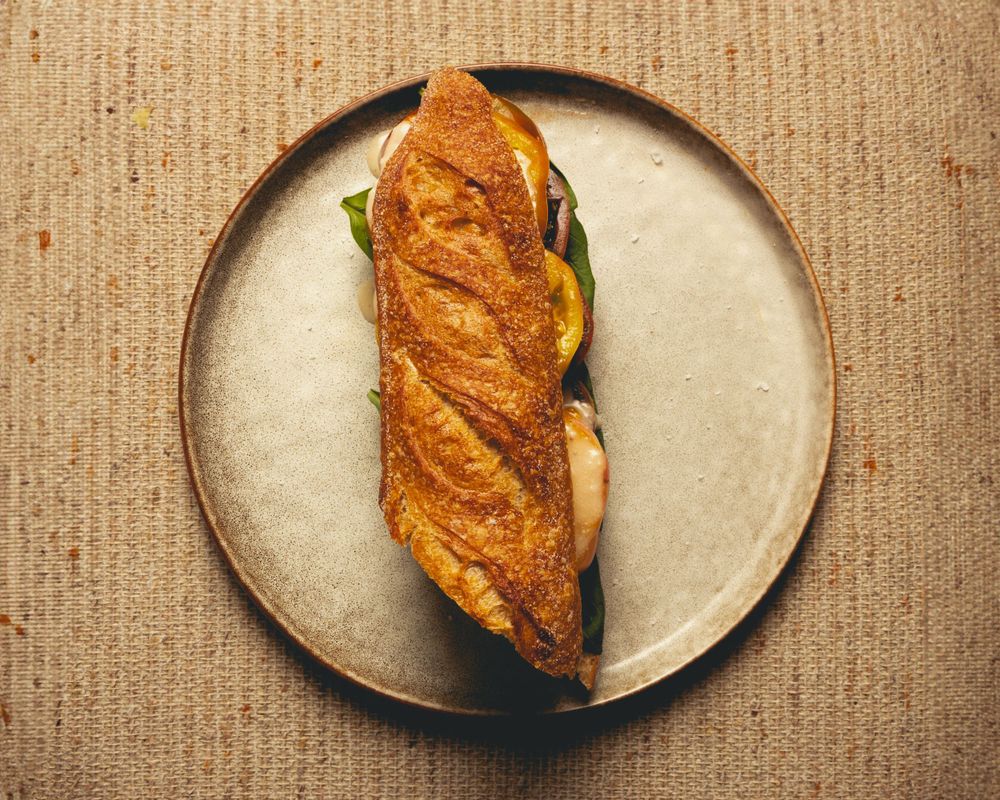 Golden brown baguette sandwich with fillings on round ceramic plate against textured background.