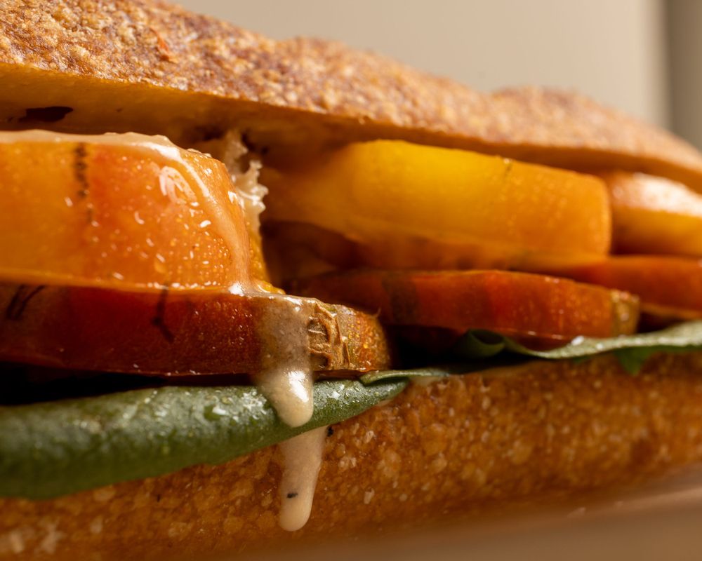 Close-up of a layered sandwich with fresh vegetables and meat between toasted bread slices.