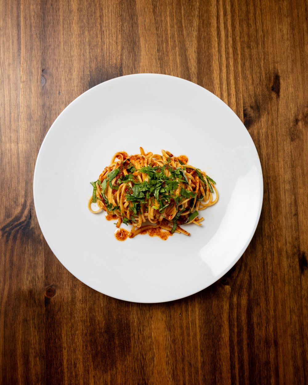 Pasta with red sauce and herbs served on a white plate against wooden background.