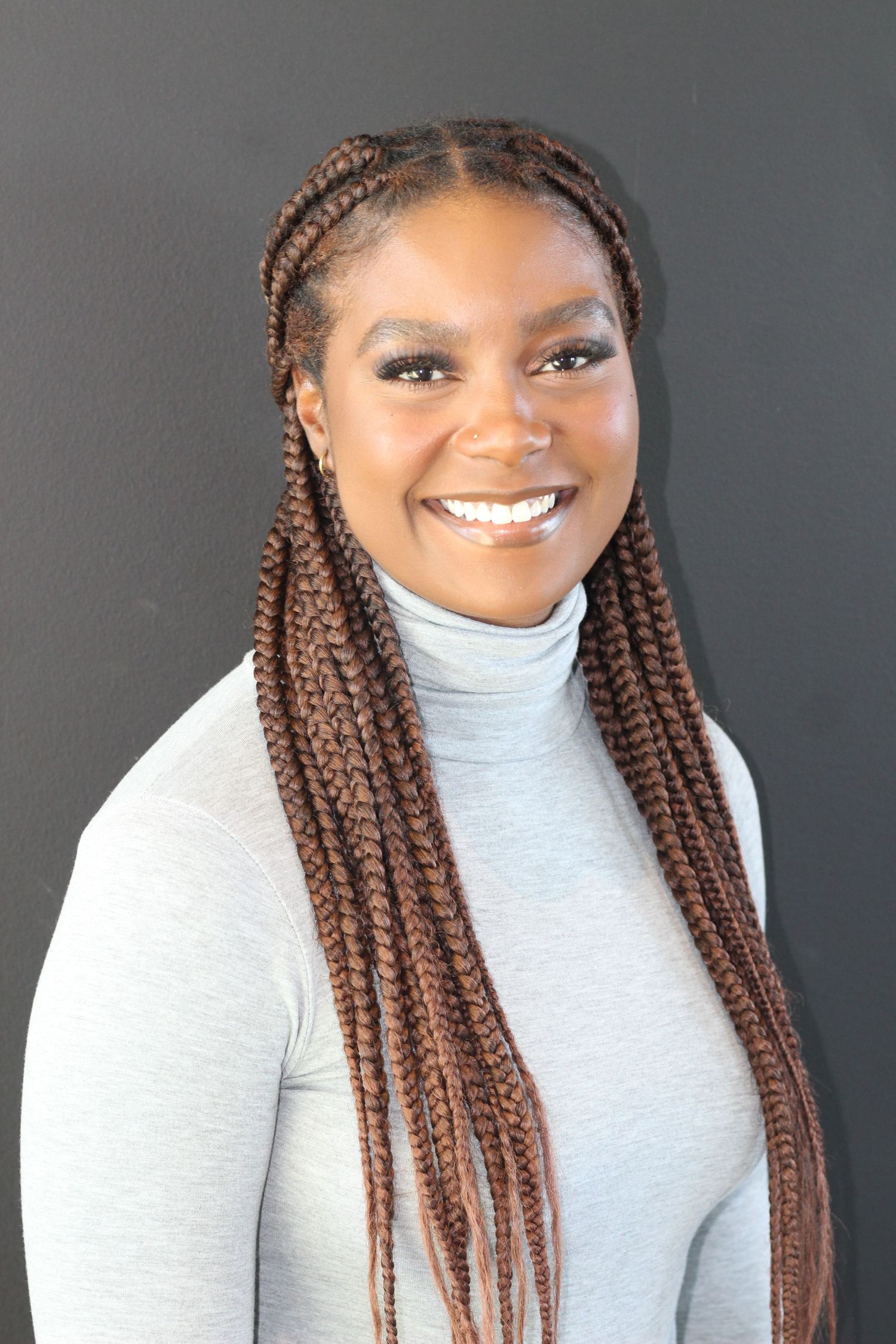 Professional portrait of someone wearing a white turtleneck sweater with long braided hairstyle against dark background.