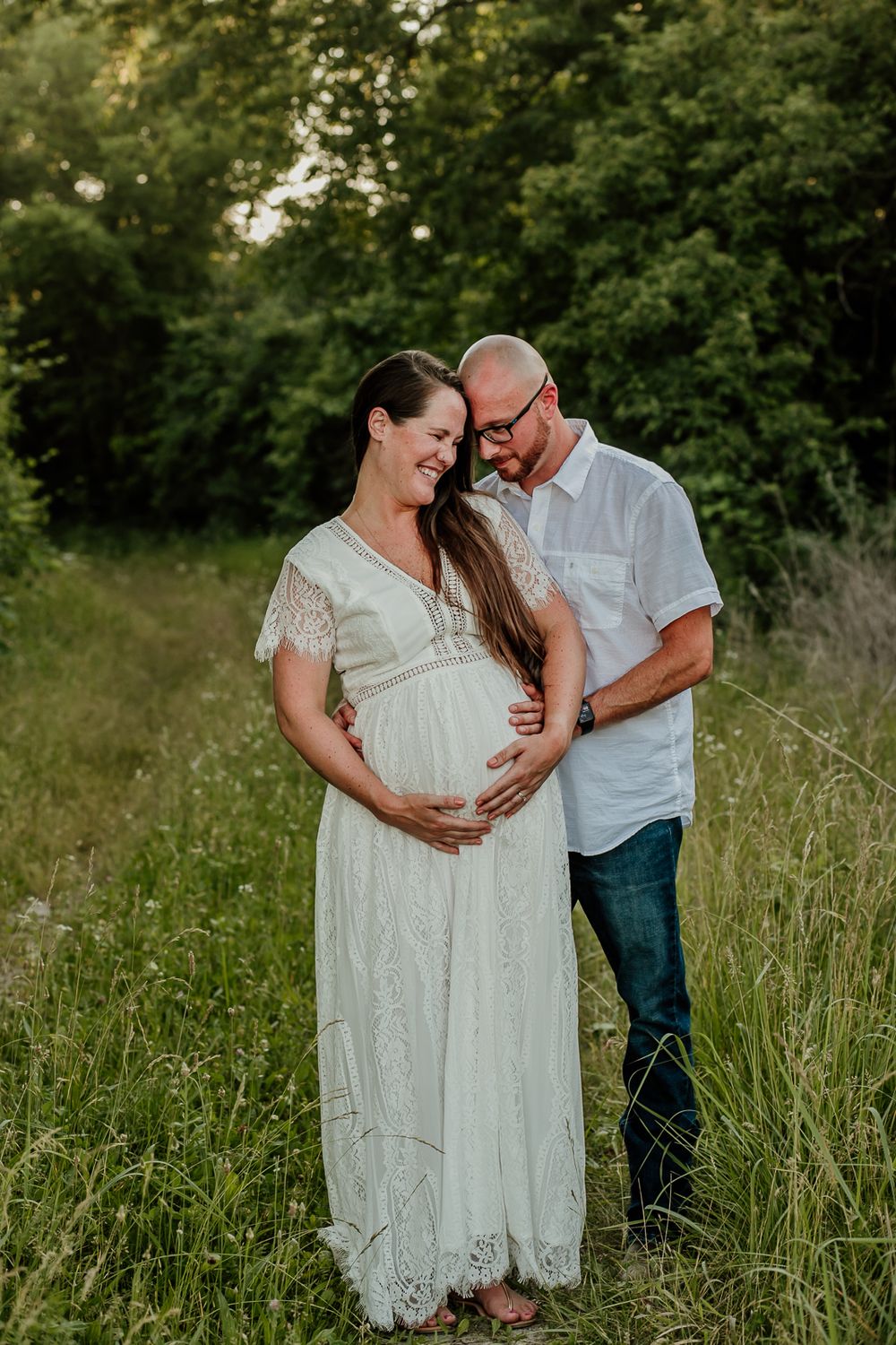 Natural maternity photos of couple laughing together in summer meadow.