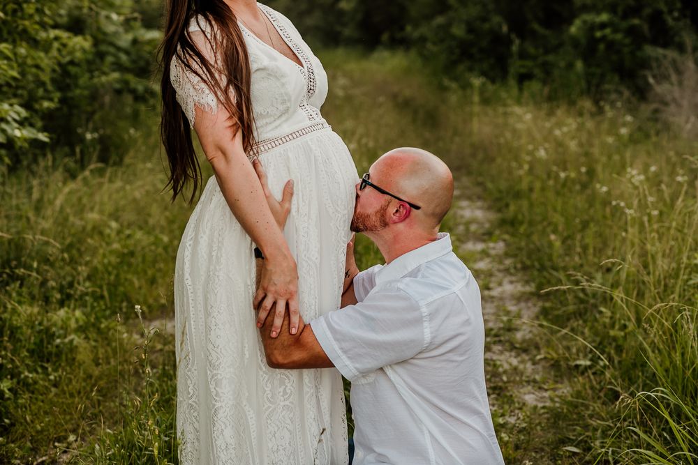 Intimate maternity session with couple in white dress and casual wear outdoors.
