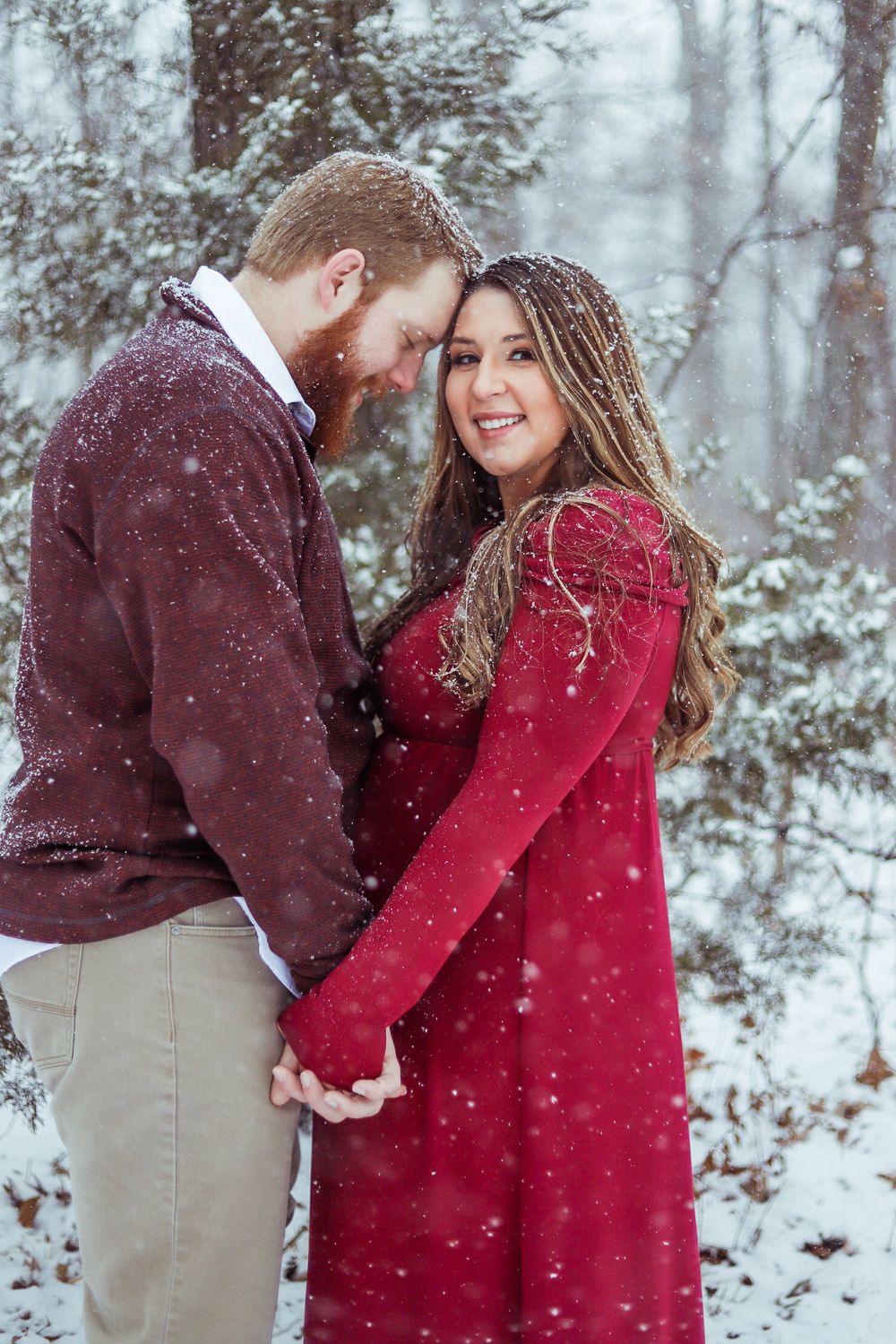 Romantic winter couple photoshoot with falling snow and red sweater in snowy forest.