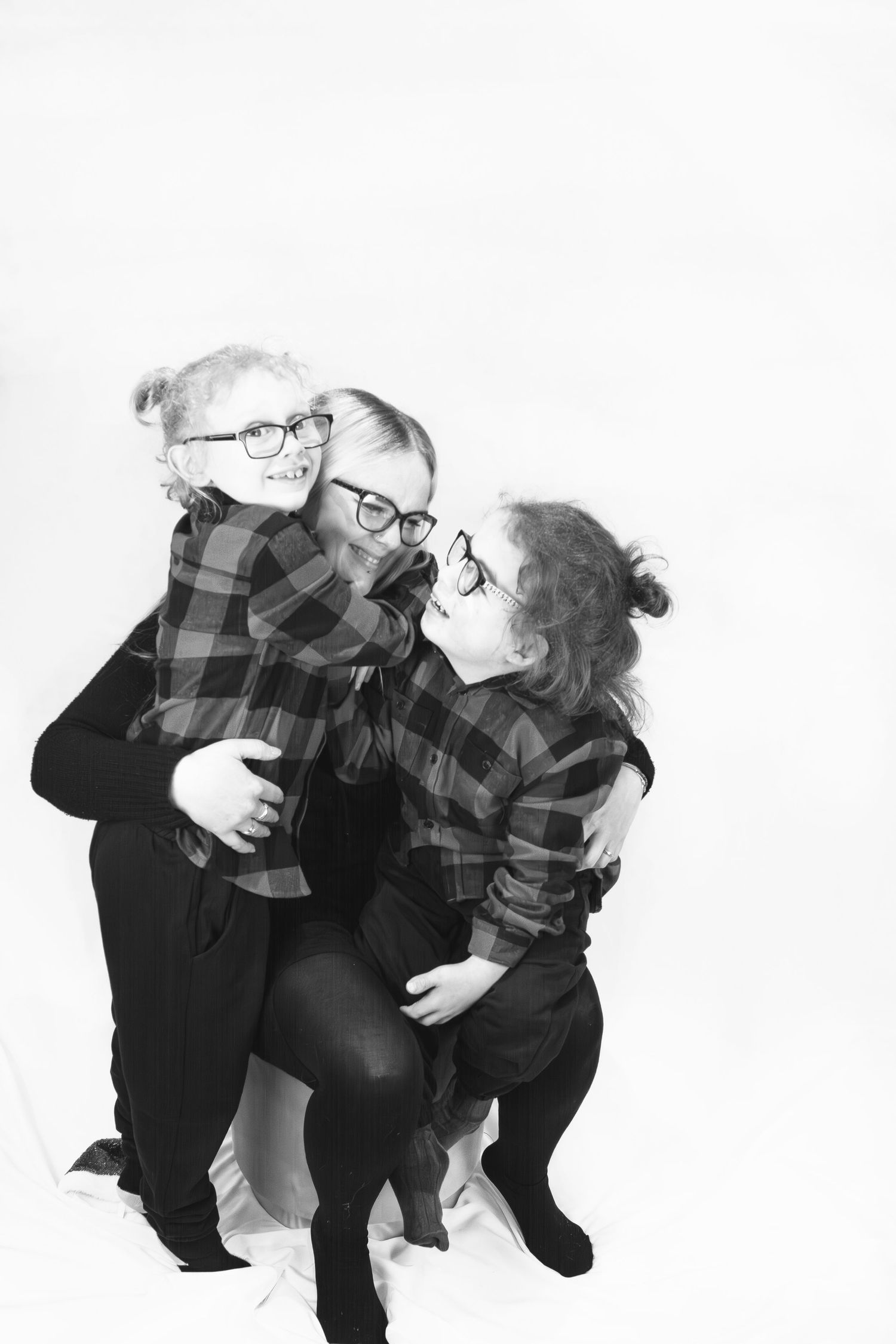 Black and white photo of three children in matching plaid shirts and glasses laughing together.