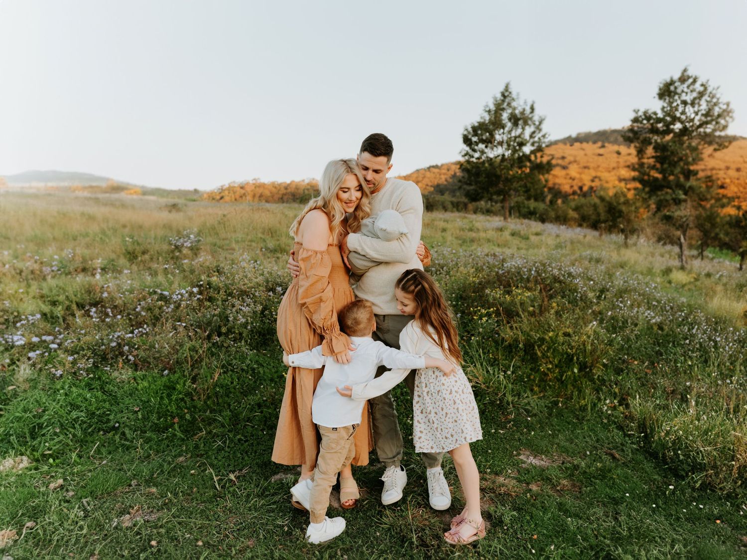 A family embraces on a grassy hilltop during golden hour with mountains in the background.