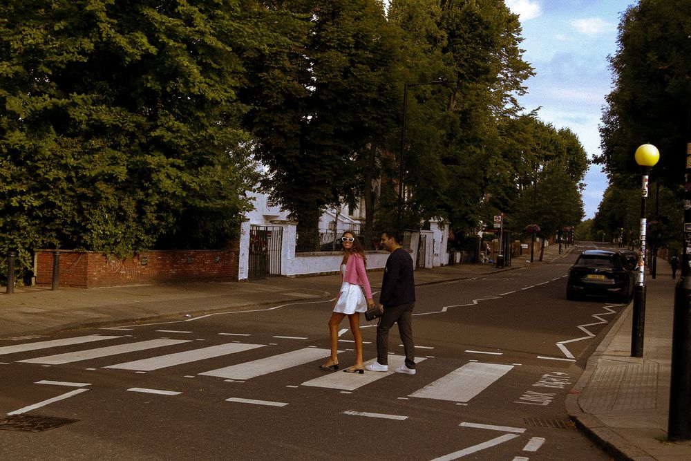 Couple walking across Abbey Road style pedestrian crossing on sunny day.