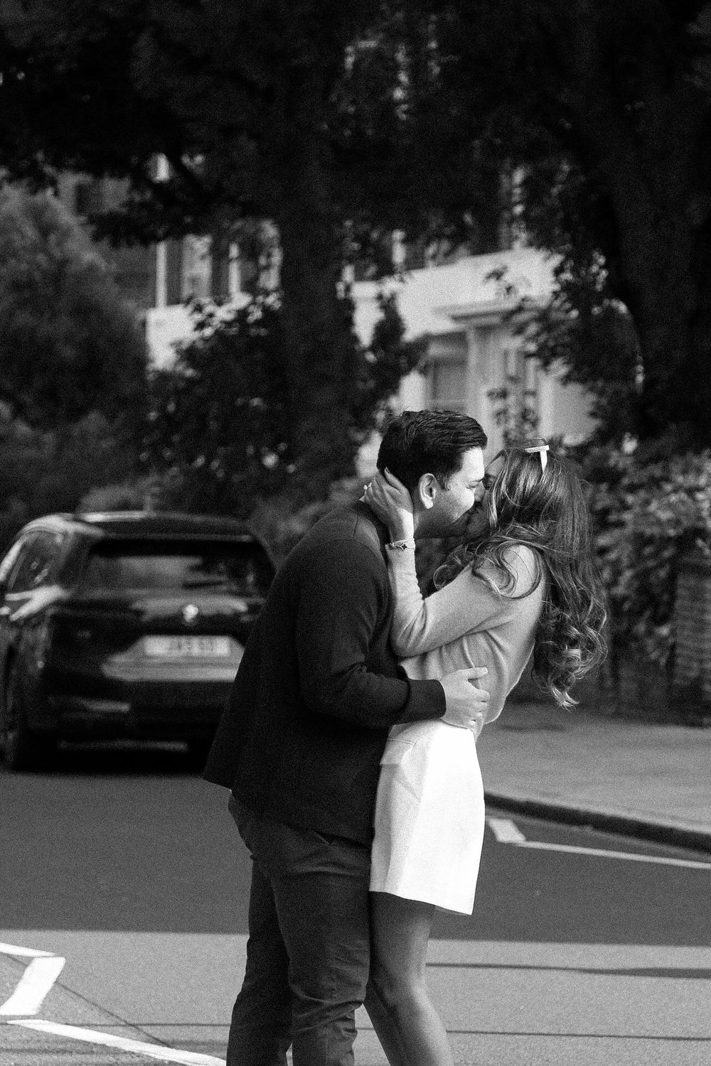 A black and white photograph capturing an intimate moment between a couple on a city street.