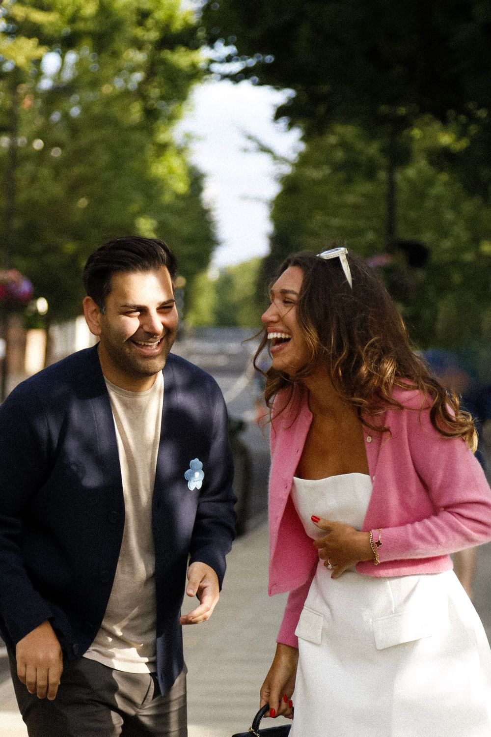 A joyful couple sharing a candid laughing moment while walking together outdoors in casual elegant attire.