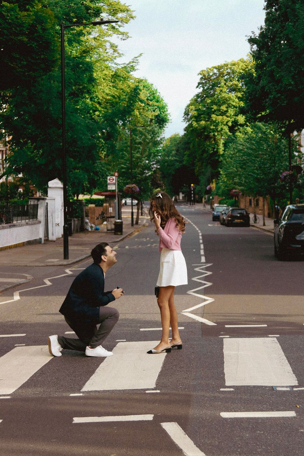 A romantic proposal scene on a zebra crossing with trees lining a quiet residential street.