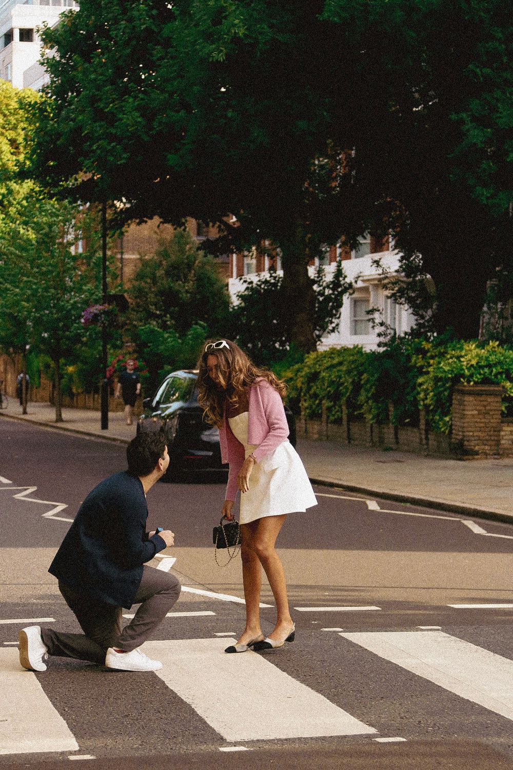 A surprise proposal taking place on a zebra crossing in a tree-lined neighborhood.