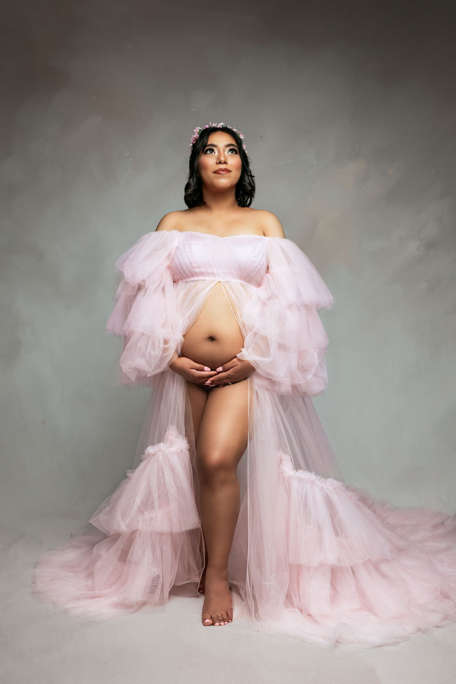 Maternity portrait with flowing pink tulle gown against grey backdrop.