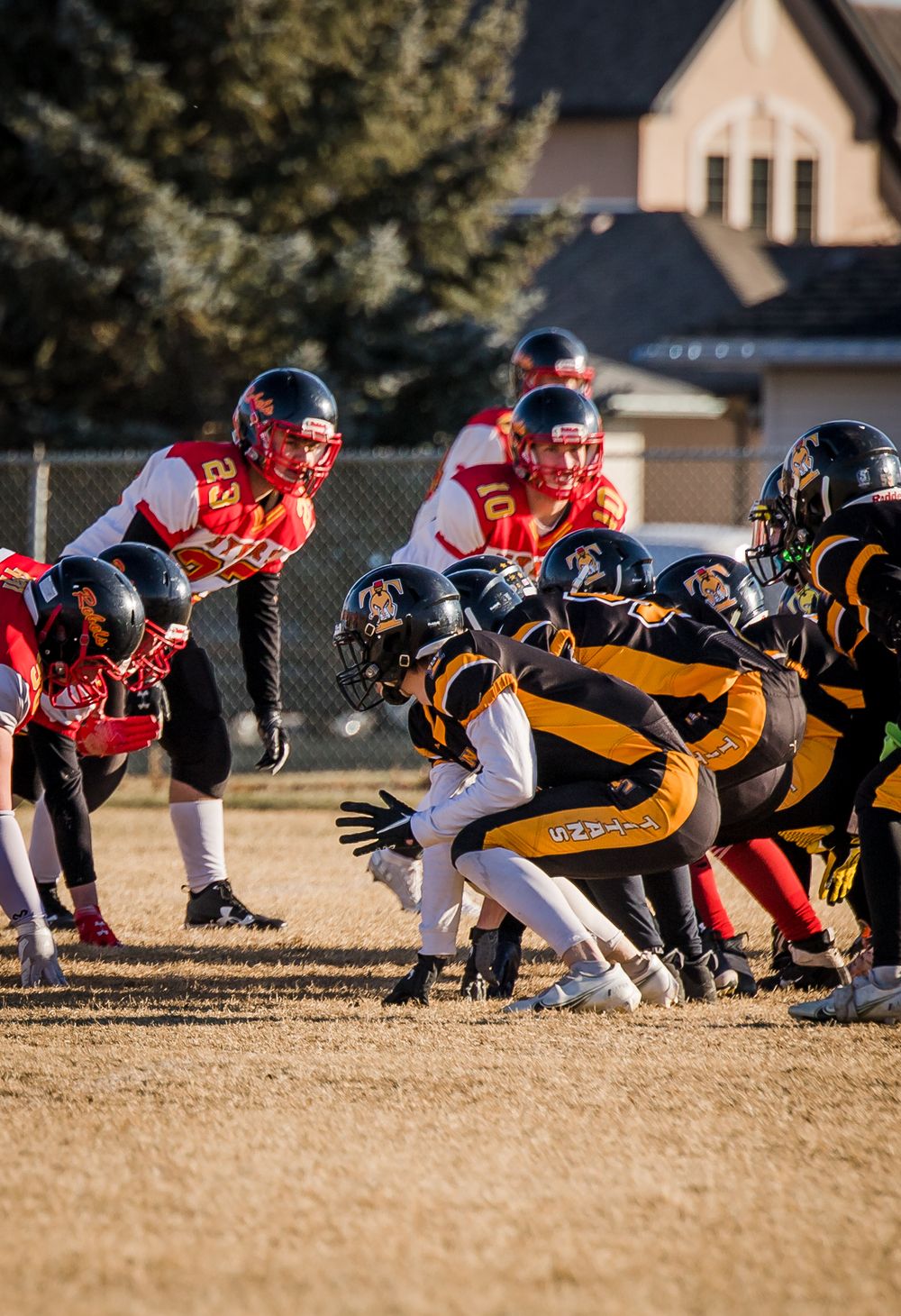Football players in red and black-yellow uniforms face off at line of scrimmage during afternoon game.