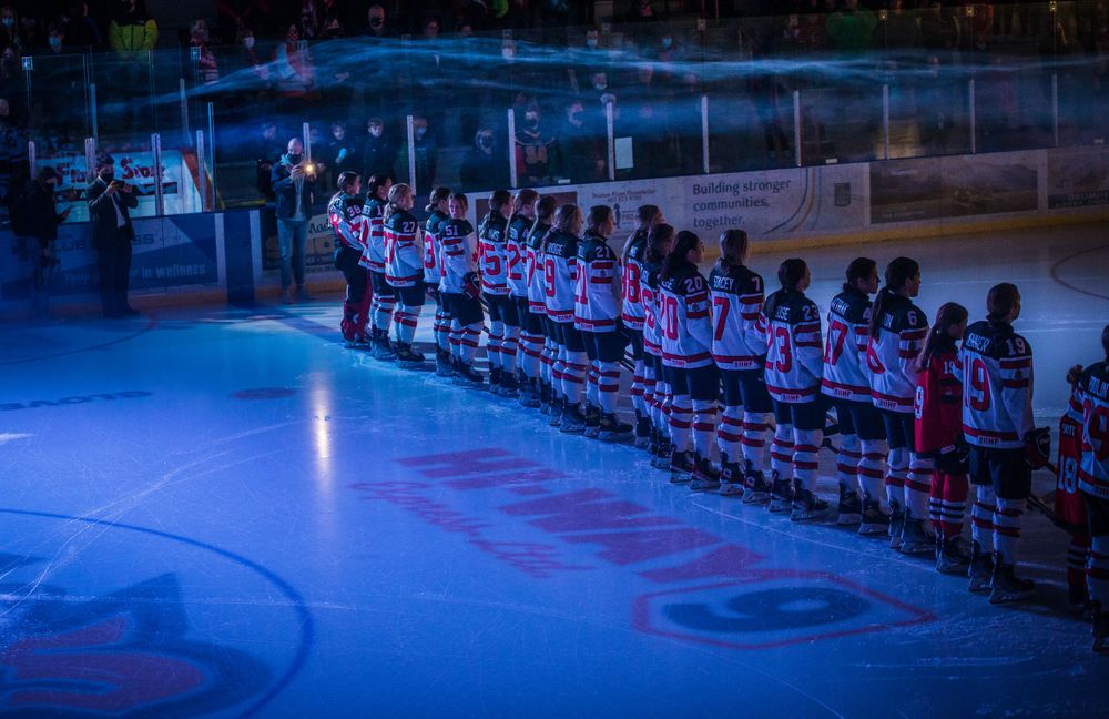 Hockey players stand in formation under blue lighting for pre-game ceremony on ice.