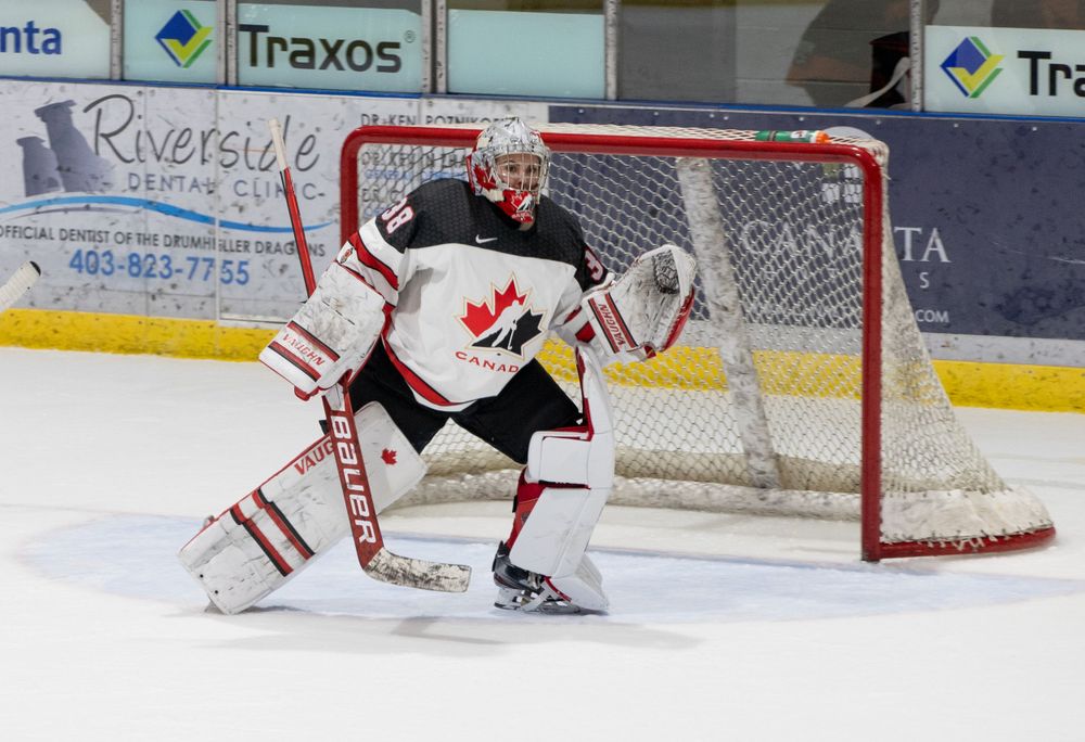 Hockey goalie in white and red uniform crouches in ready position at the net.