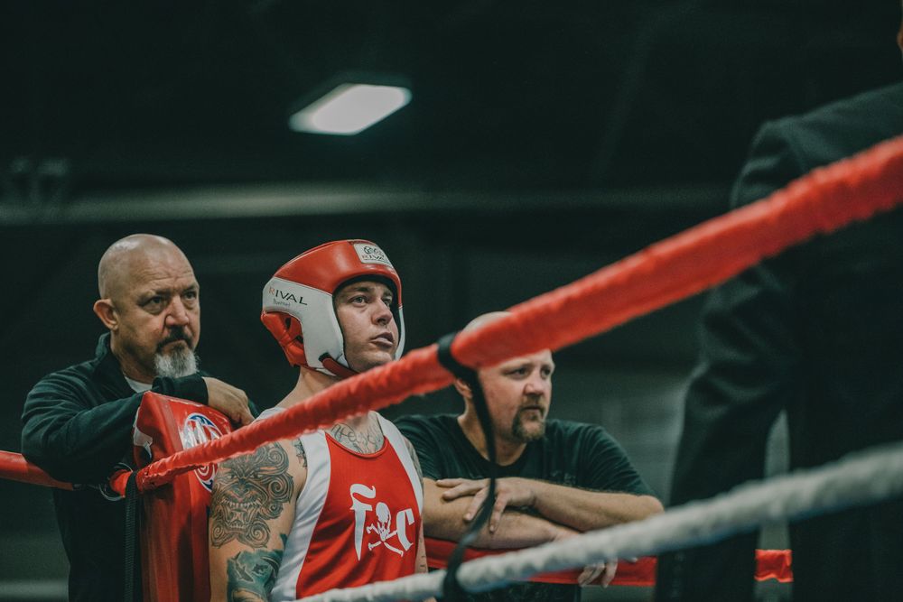 Boxer in red headgear and coaches at ringside during match.