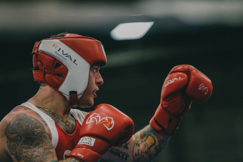 Boxer in red headgear and gloves with visible tattoos in fighting stance.