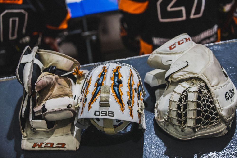Collection of white hockey goalie masks and equipment displayed on blue surface.