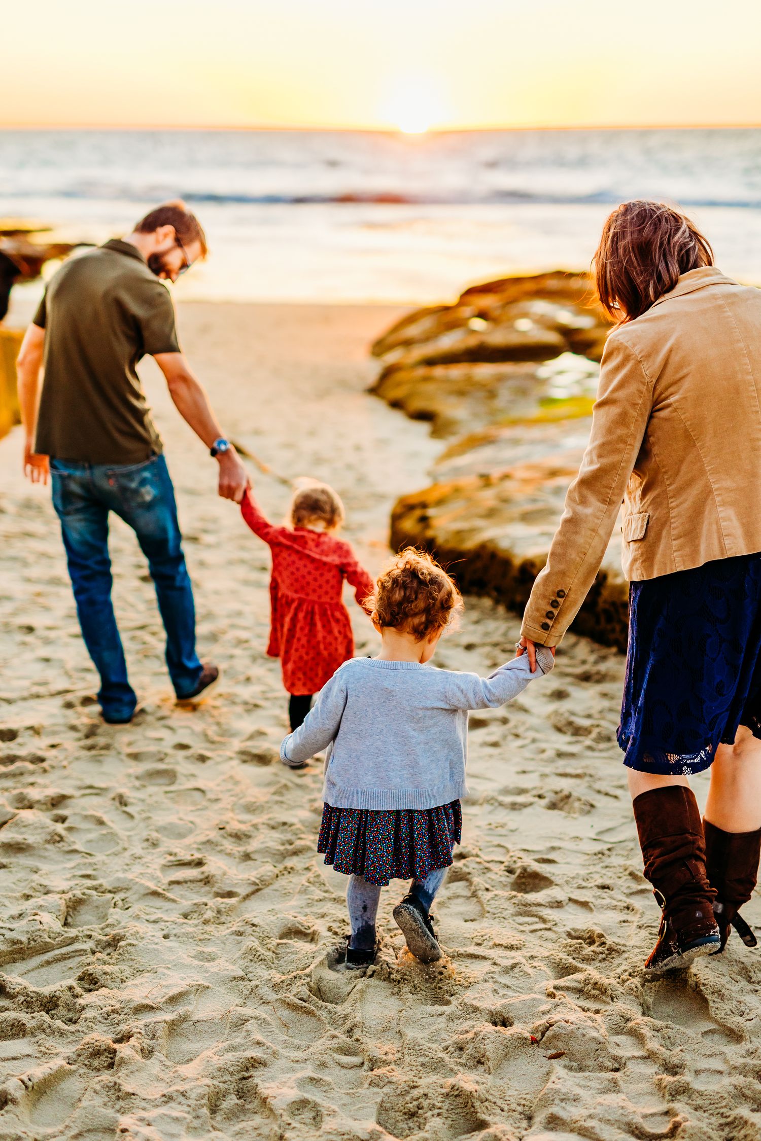 Young family walks towards the ocean during golden hour beach photography session in La Jolla, California.