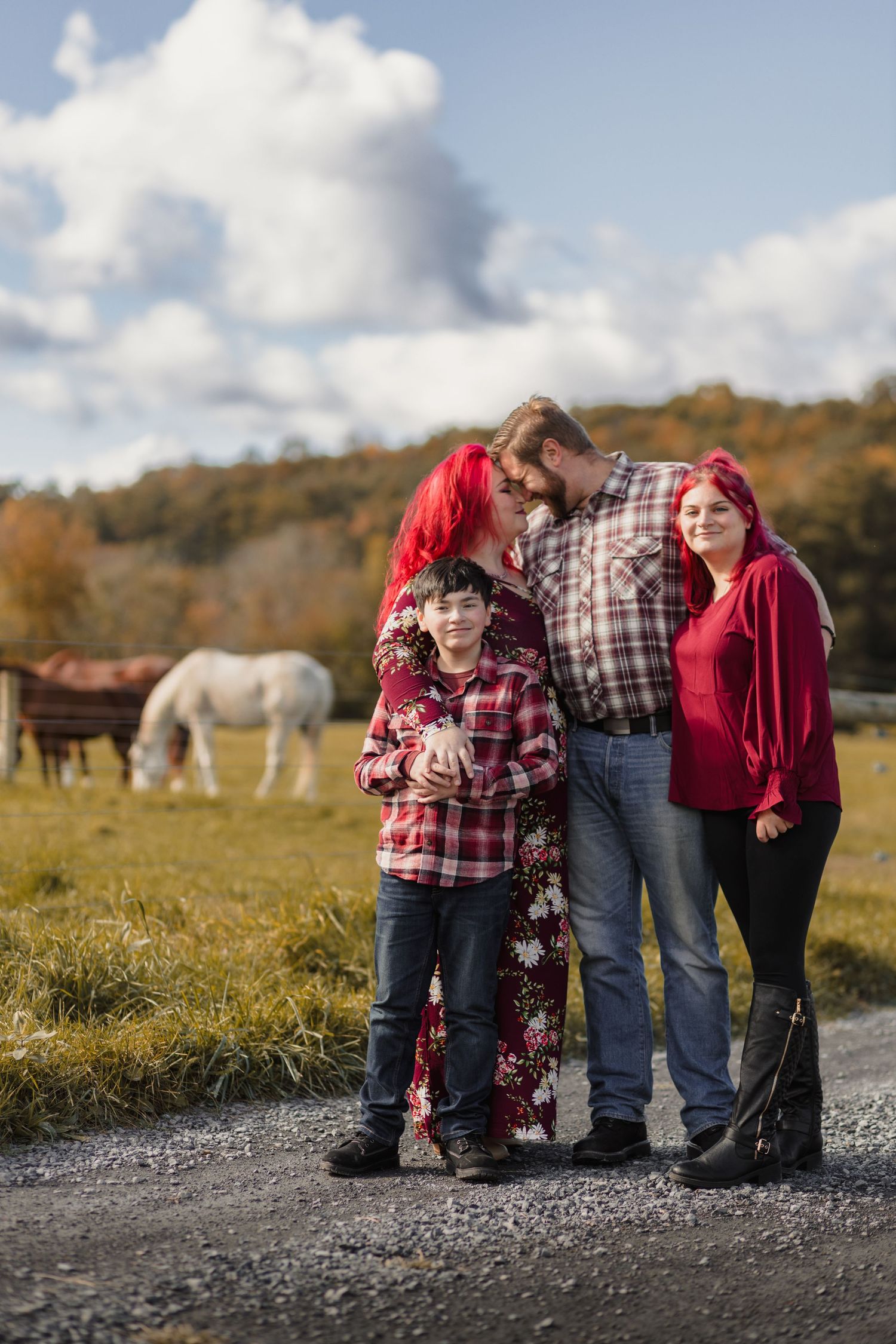 Family group poses on gravel path with horses grazing in background.