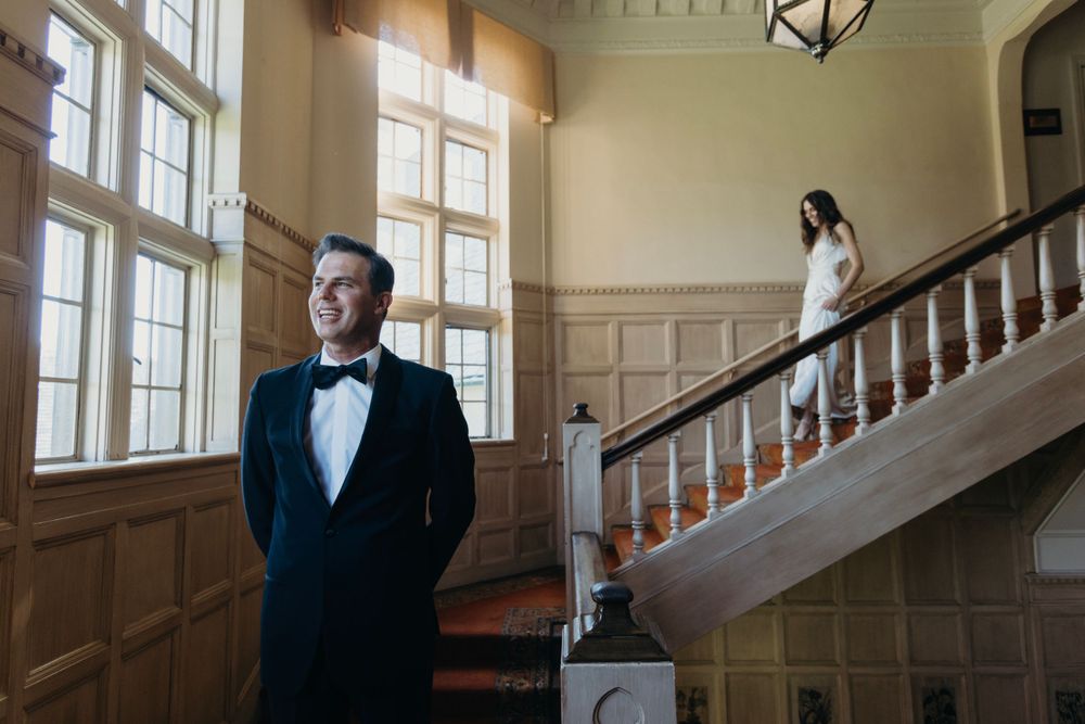 Elegant wedding first look moment in a historic building with wood paneled walls and tall windows.