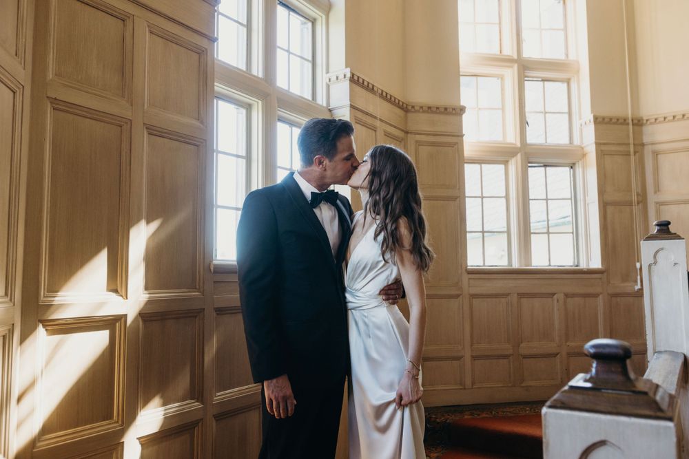 Romantic wedding couple embracing in sunlit room with wood paneled walls.