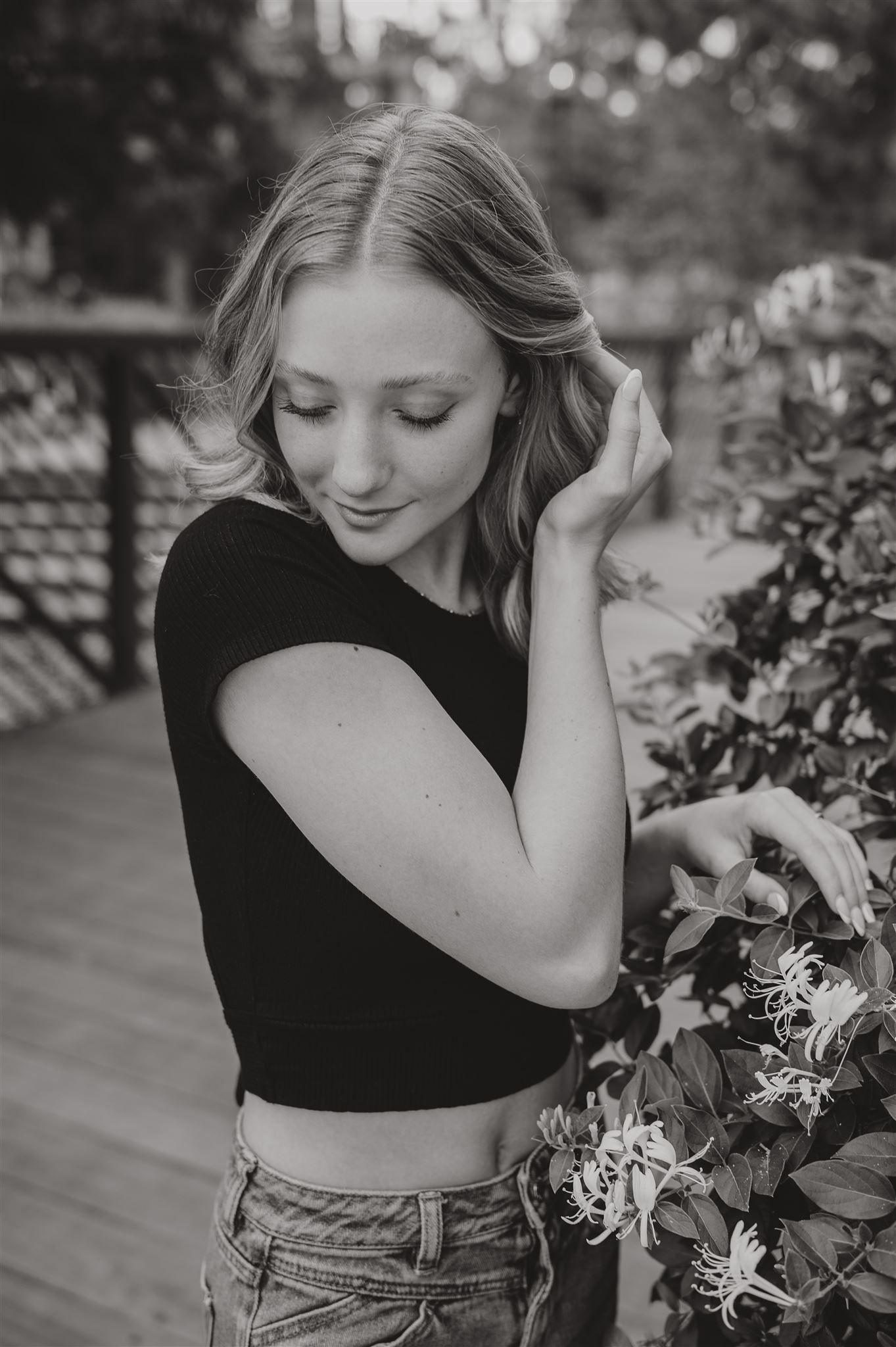Black and white portrait of a person in a crop top near decorative plants on a wooden deck.