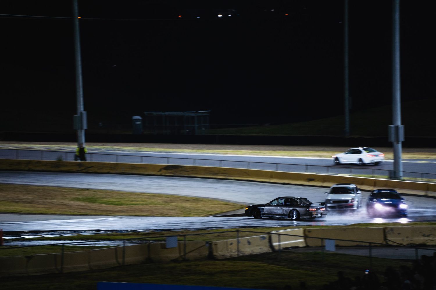 Race cars drifting on illuminated track at night with dramatic lighting.