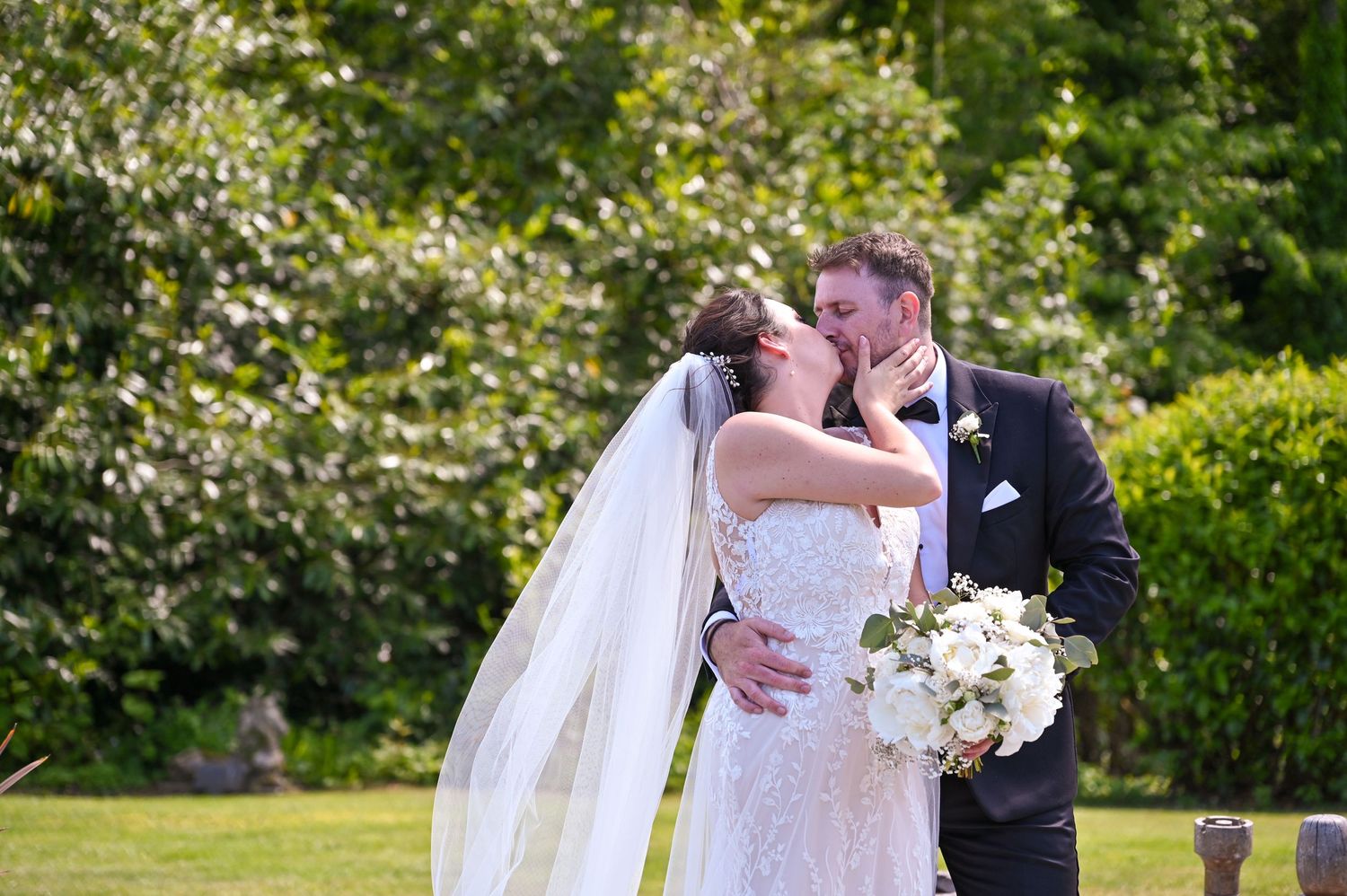 Romantic wedding moment captured in a sunlit garden with flowing white veil.