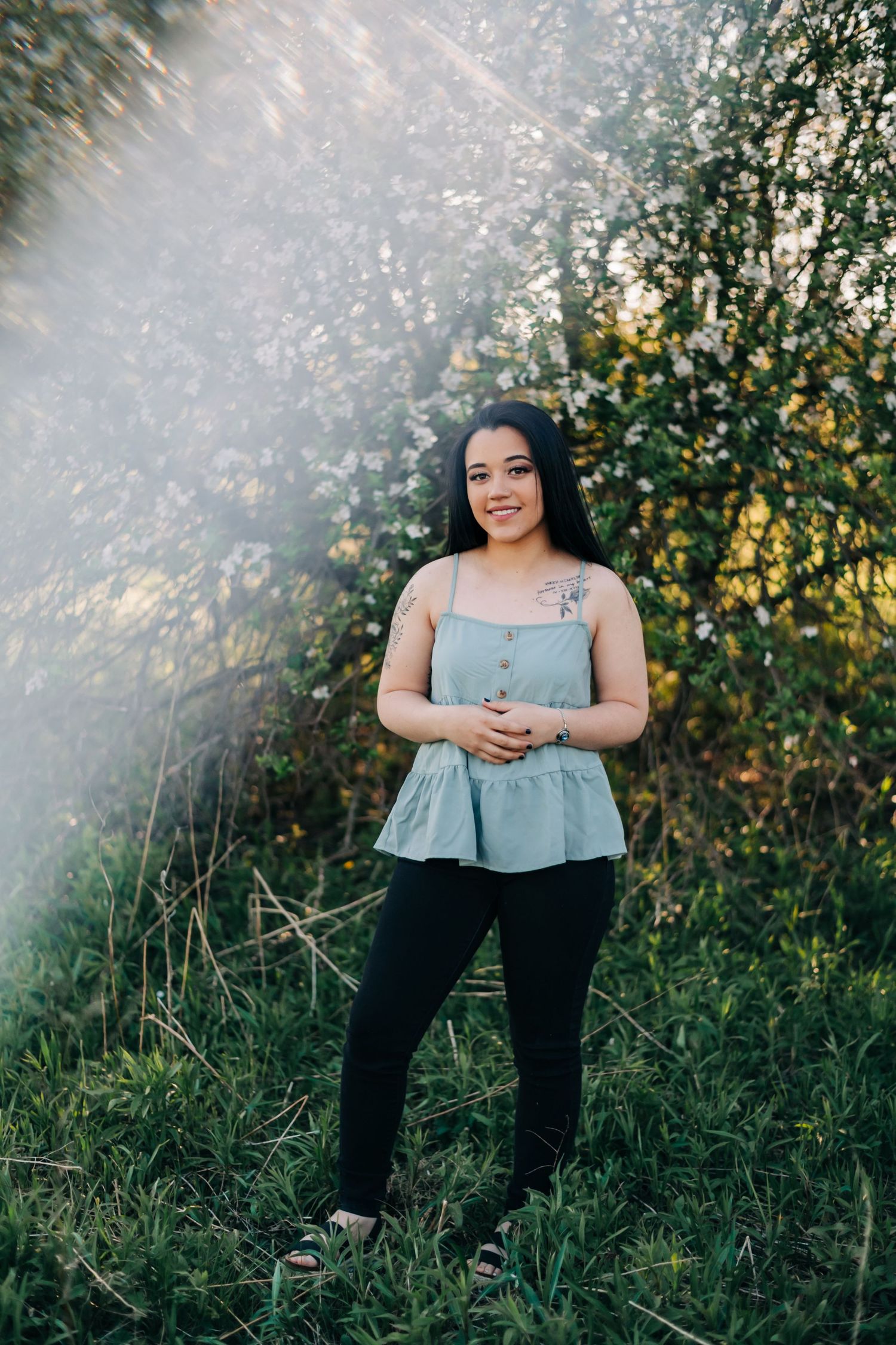 high school senior wearing a blue tank top standing in front of a blossoming apple tree