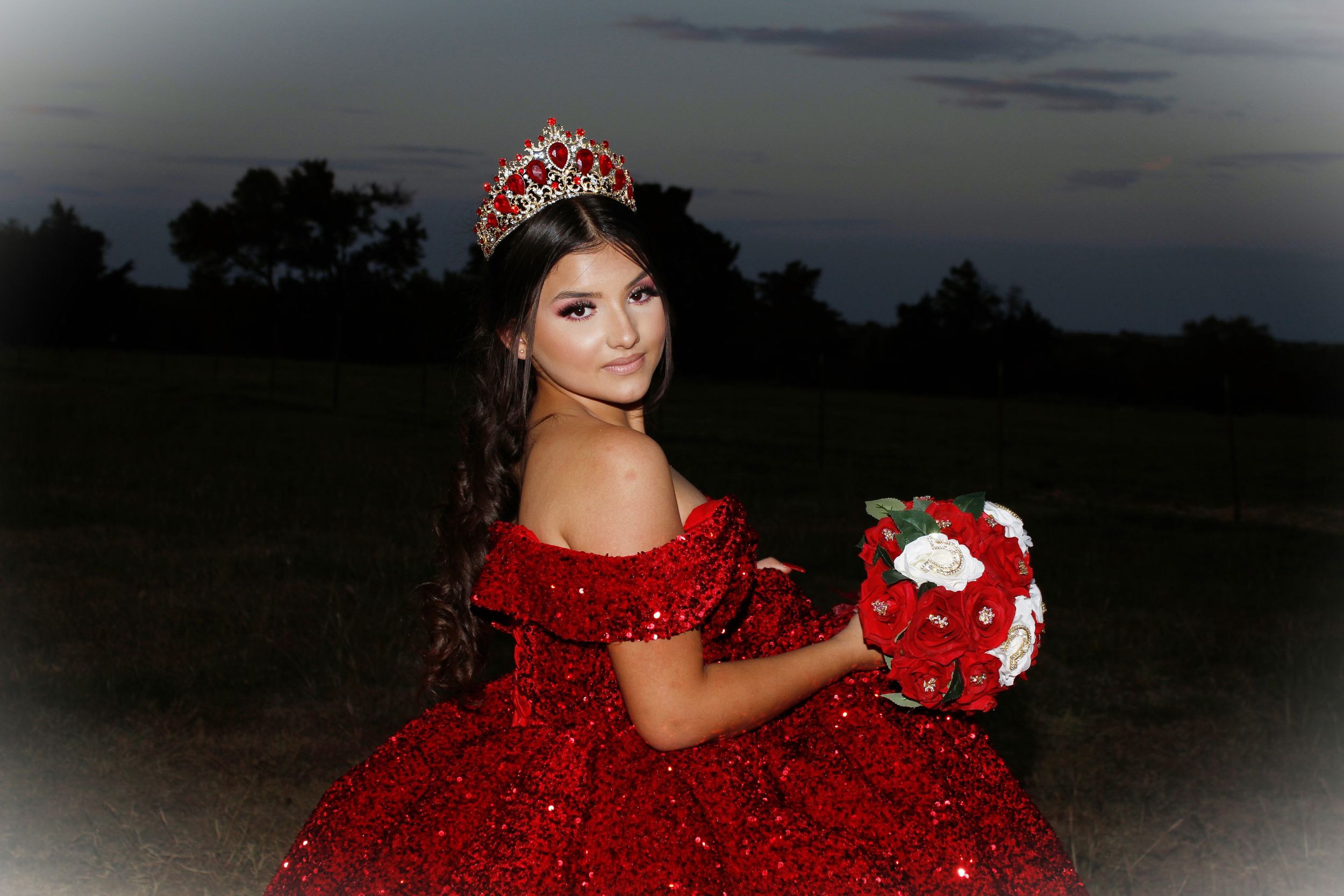 A red formal gown with bouquet photographed against a dusky evening sky.