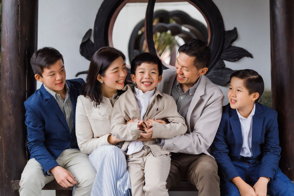 Family sitting together and sharing a joyful moment on a wooden bench under an ornate archway.